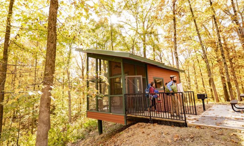 Cabin in autumn forest, two people on the deck enjoying the view.