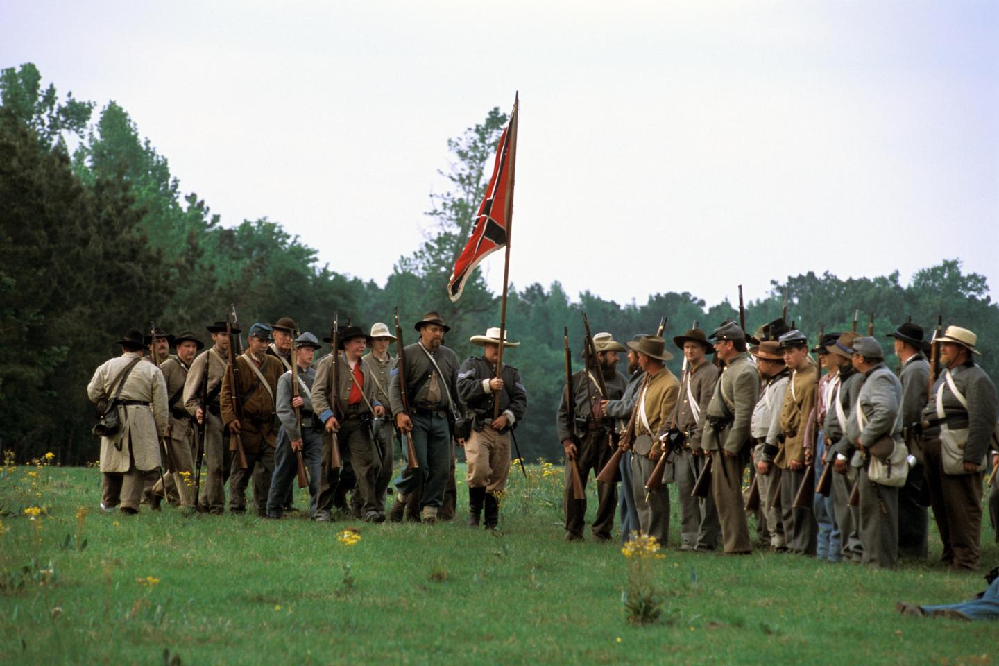 Civil War reenactors gather on a grassy field with a flag.