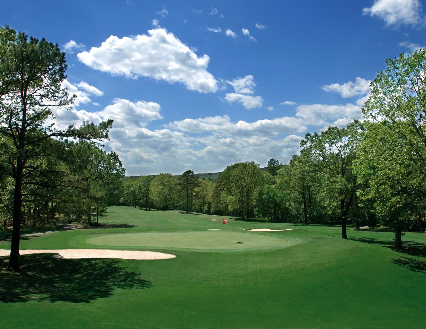 Golf course with lush green fairway, sand bunkers, and blue sky.