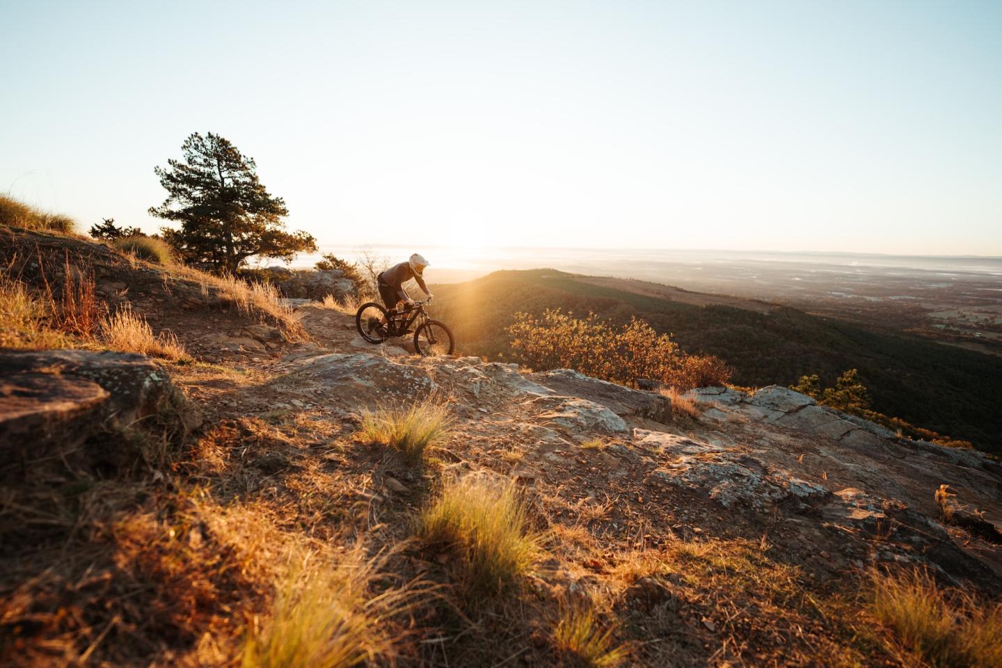 Mountain biker riding at sunset on a rocky hilltop.