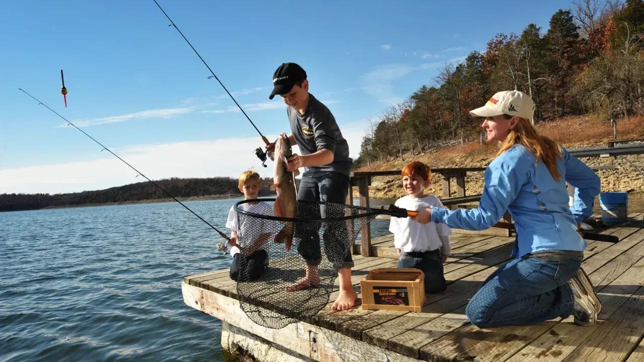 Family fishing on a wooden dock by a sunny lake.