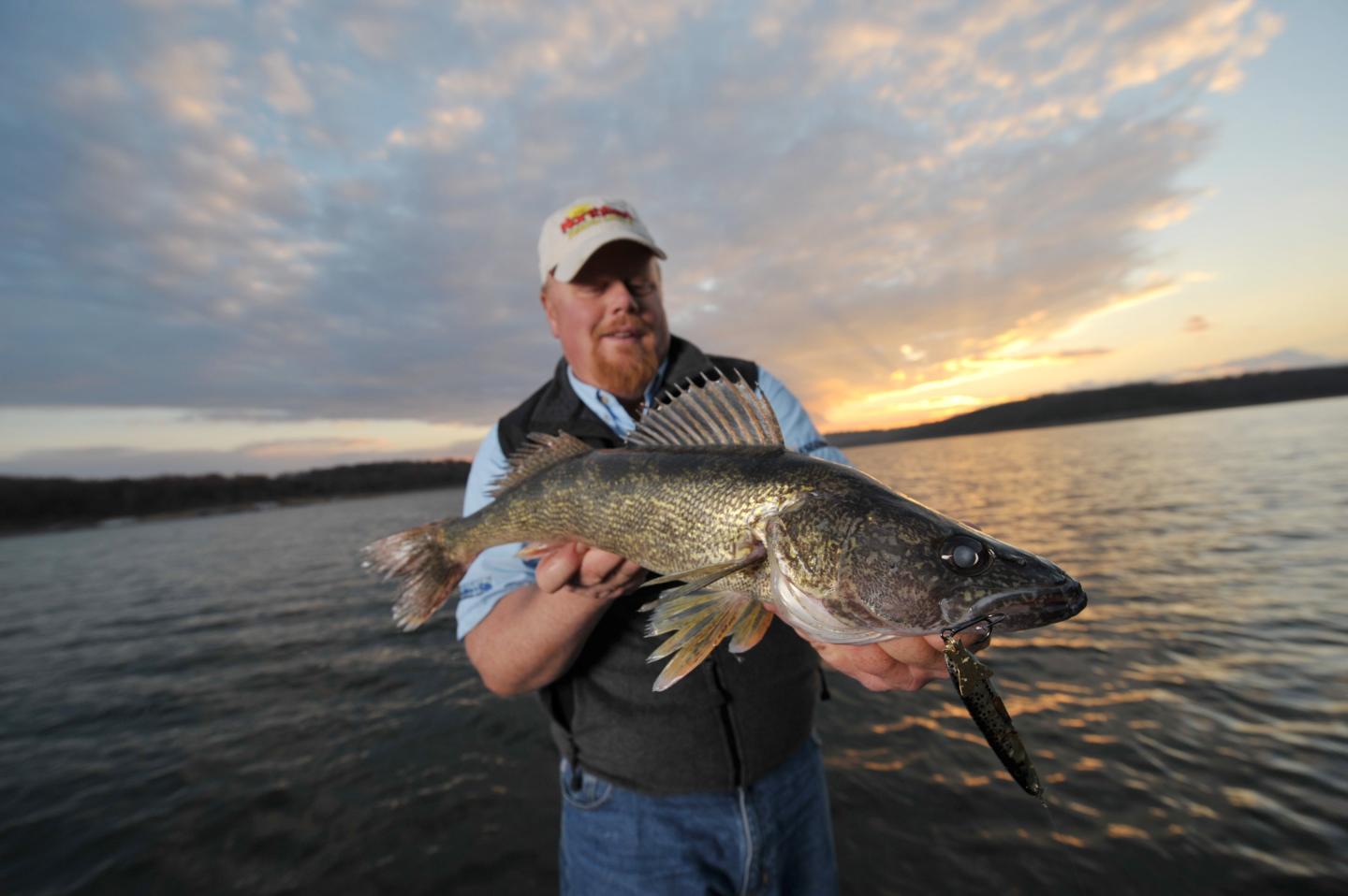 Man holding a large fish at sunset by the lake.