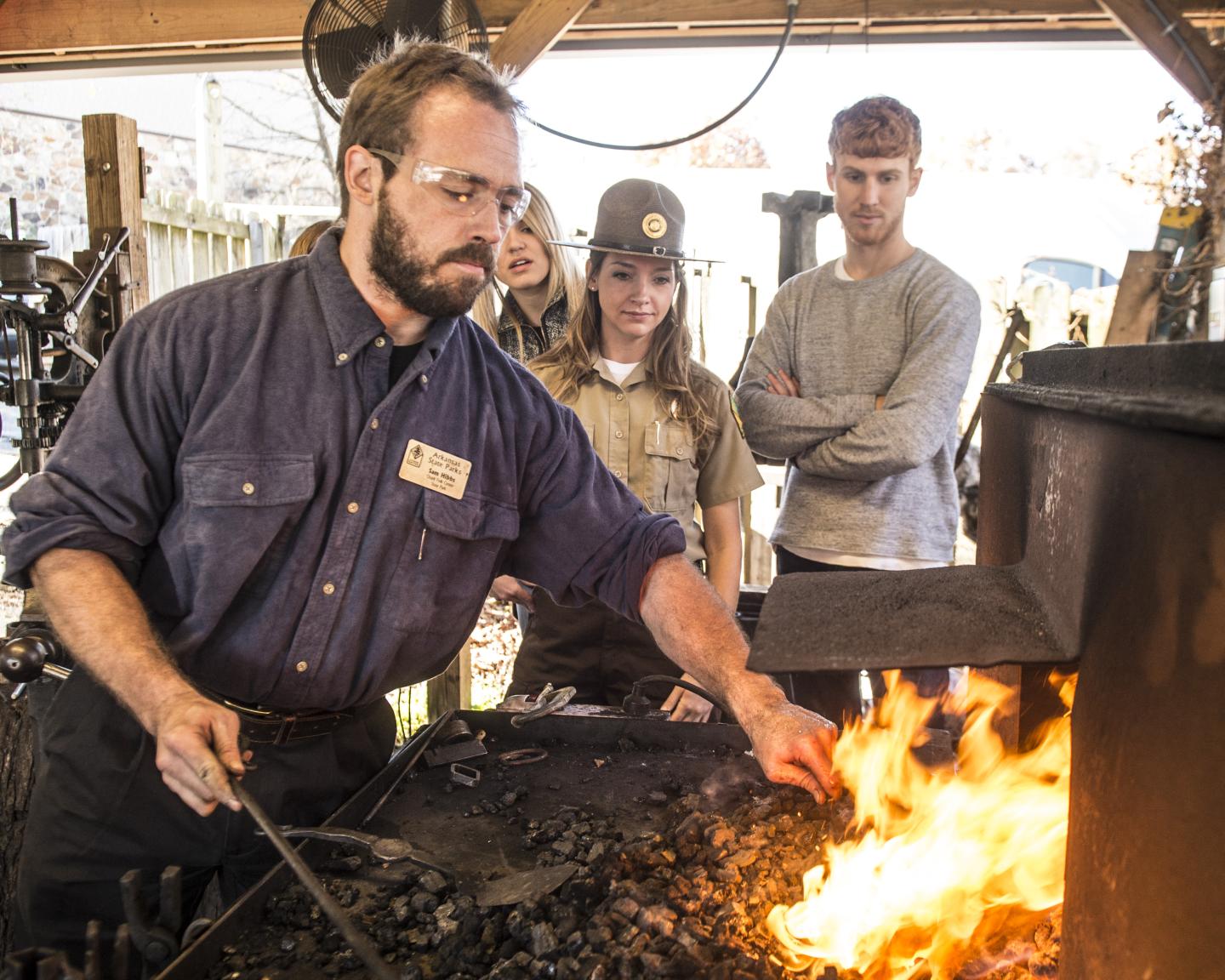 Blacksmith shaping metal in a forge, observed by visitors.