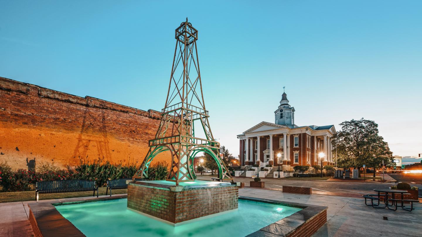 Steel tower sculpture by a fountain, historic building in background, twilight setting.