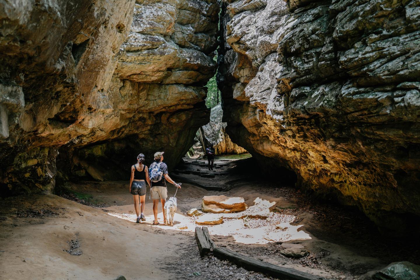 Two people exploring a sunlit rocky cave.
