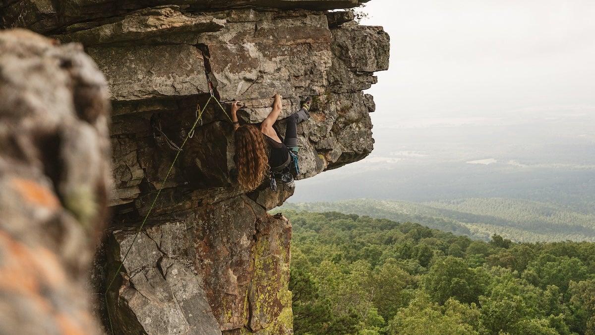 Rock climber scaling a cliff above a lush green forest.