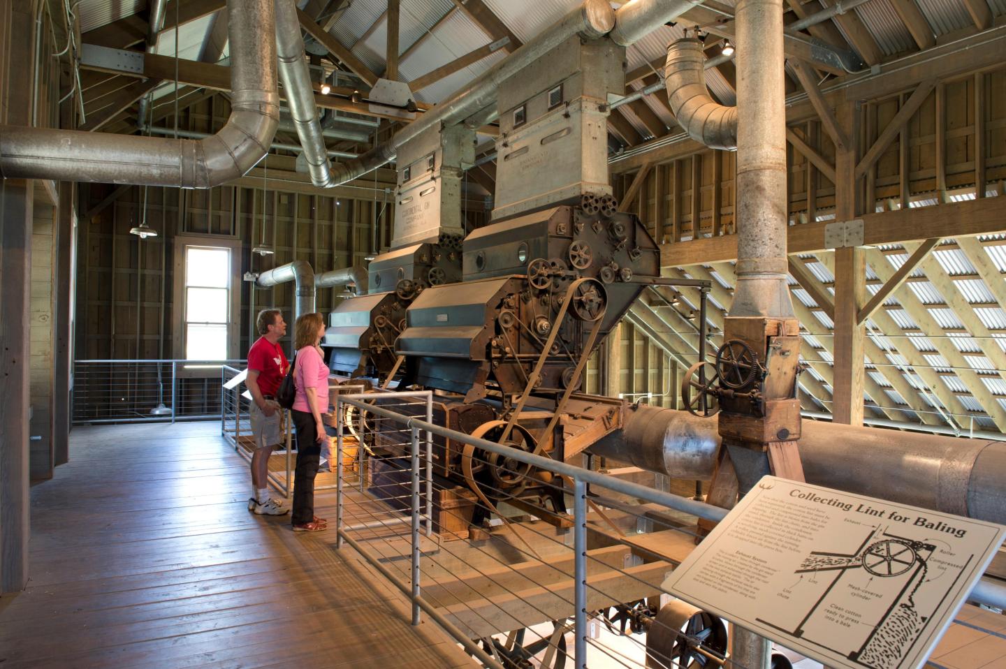 Inside a historic milling building, visitors examine machinery and diagrams.