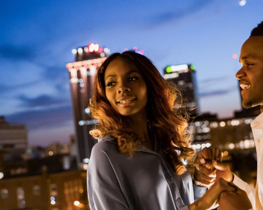 Couple on a rooftop at dusk with city lights in the background.