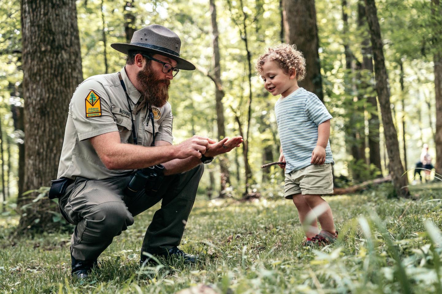 Park ranger shows bug to curious child in a forest.