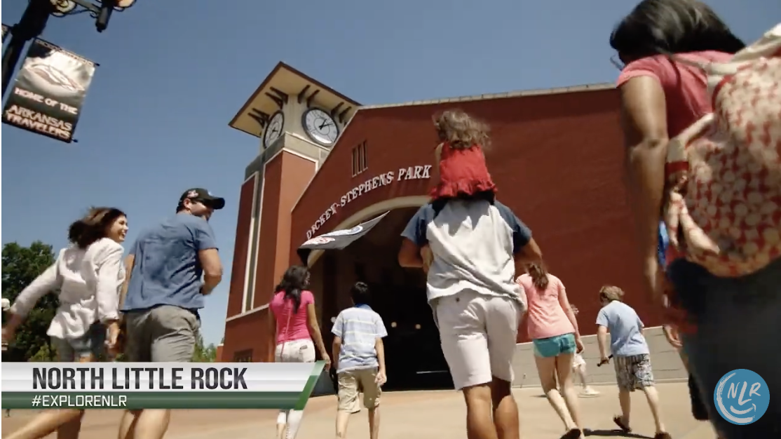 Group walking towards a brick building with a large clock under clear sky.
