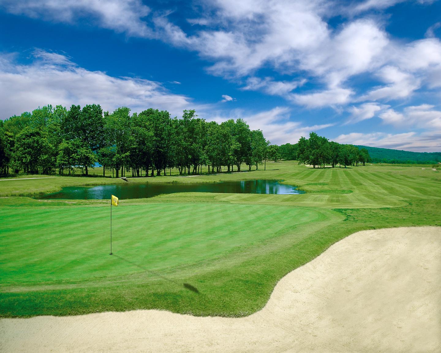 Golf course with green grass, sand trap, and blue sky.