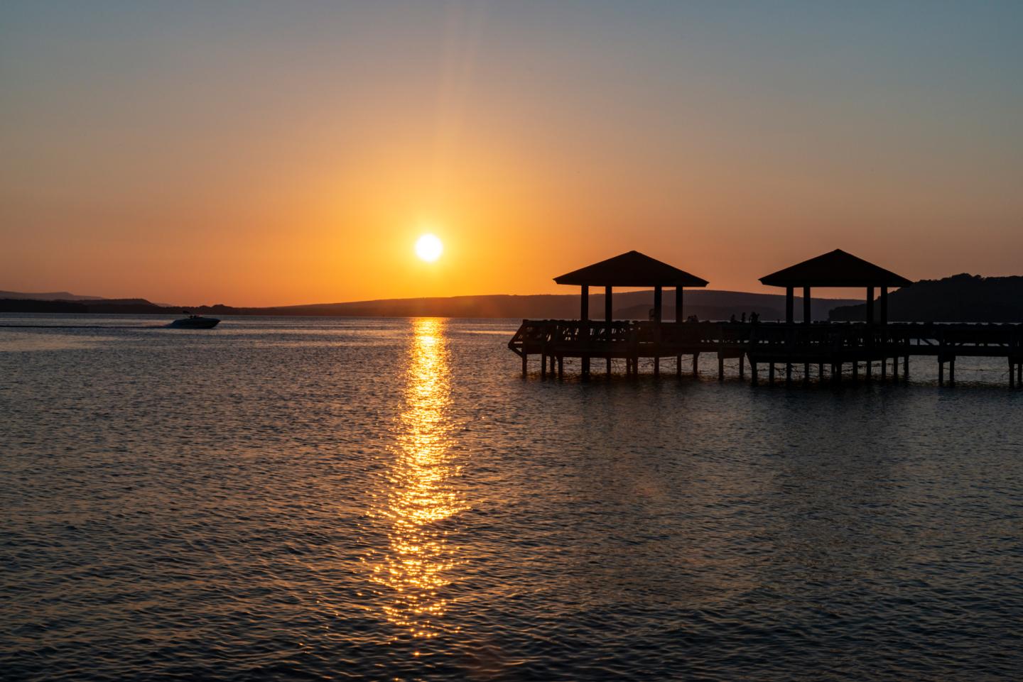 Sunset over calm water with silhouetted piers and a distant boat.