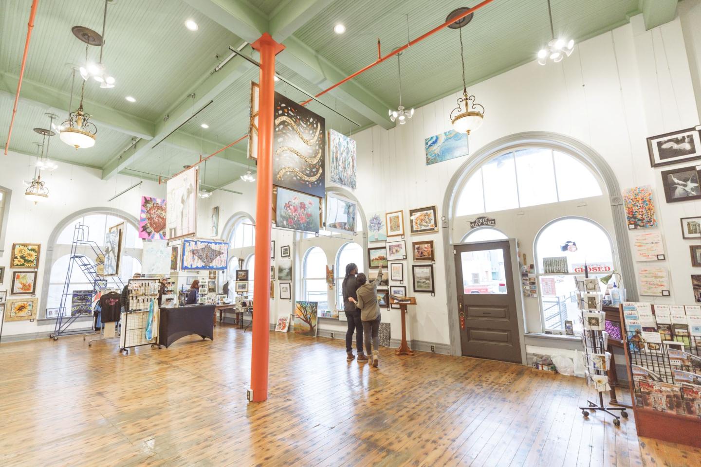 Art gallery with high ceilings, two people viewing art, eclectic paintings on walls.