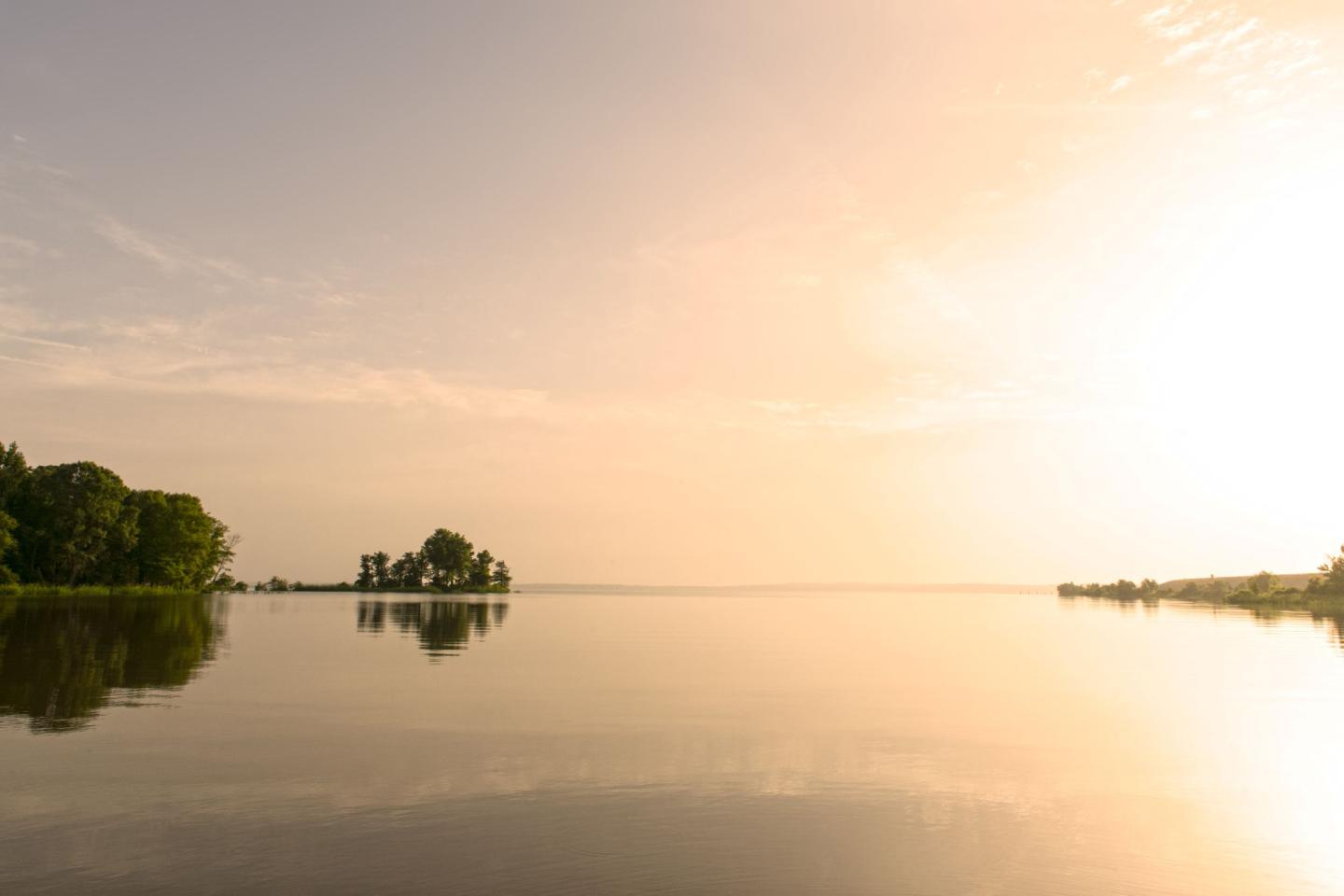 Tranquil lake at sunrise with a tree-lined shore and calm waters.