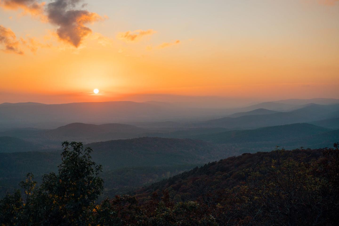 Sunset over a hilly landscape with an orange sky and scattered clouds.