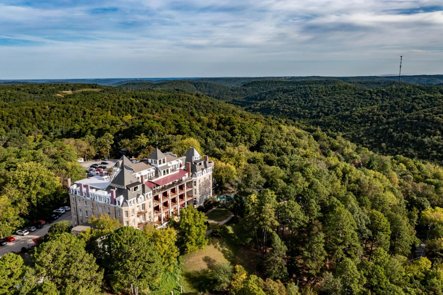 Victorian-style hotel surrounded by dense, green forest under a cloudy sky.
