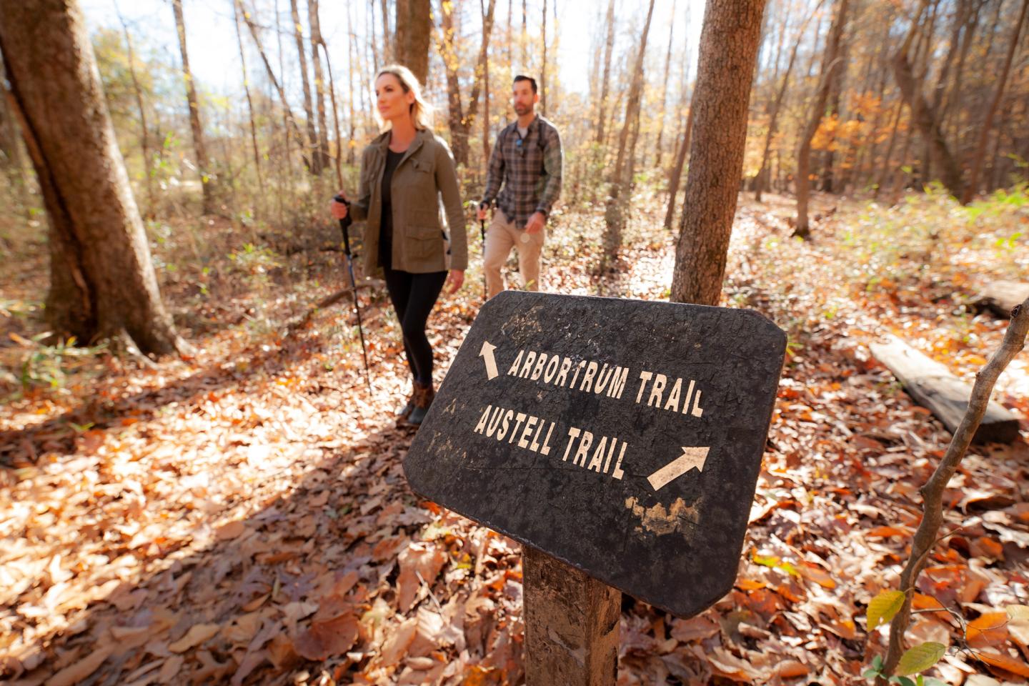 Trail sign in autumn woods with two people walking.
