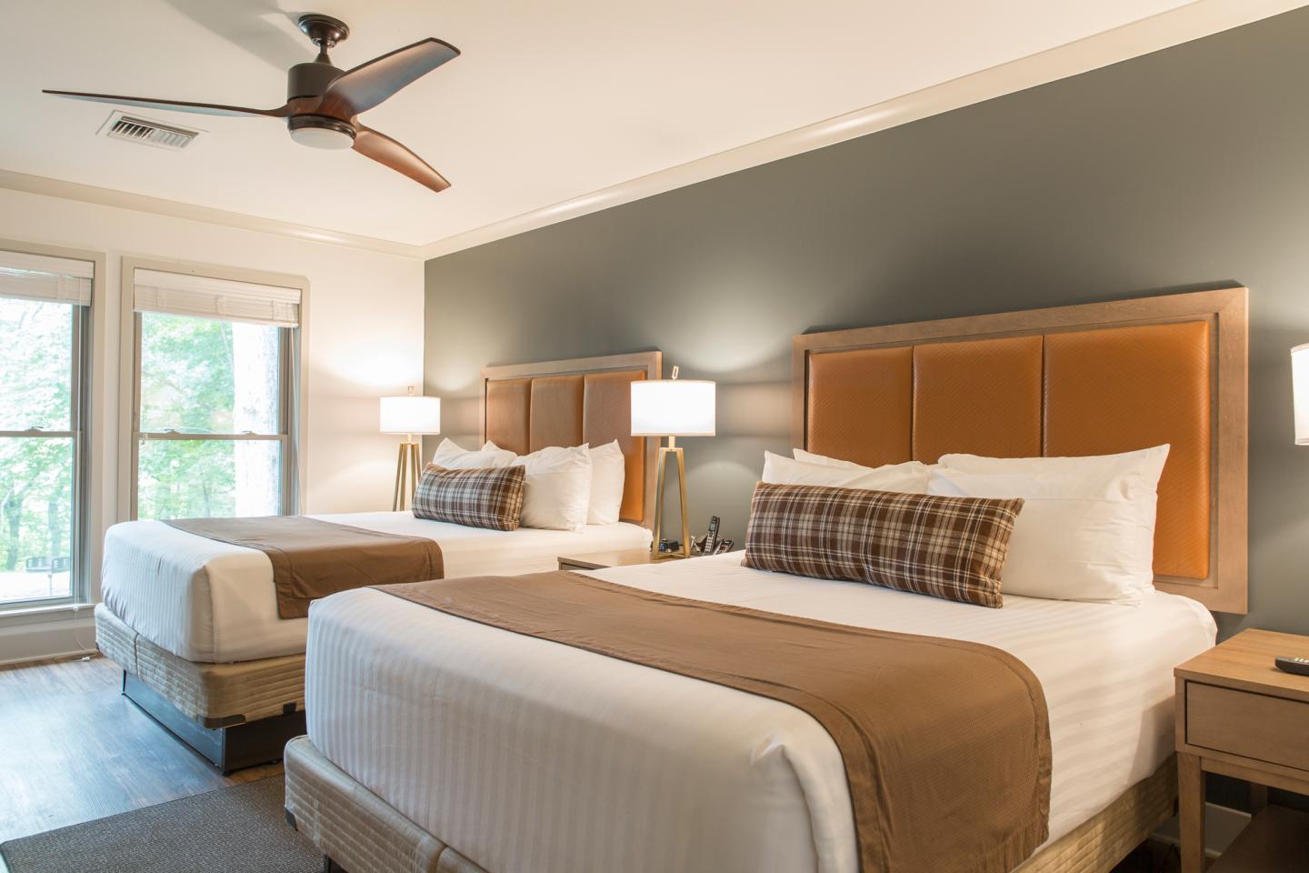 Two neatly made double beds in a lodge room with lamps and a ceiling fan.