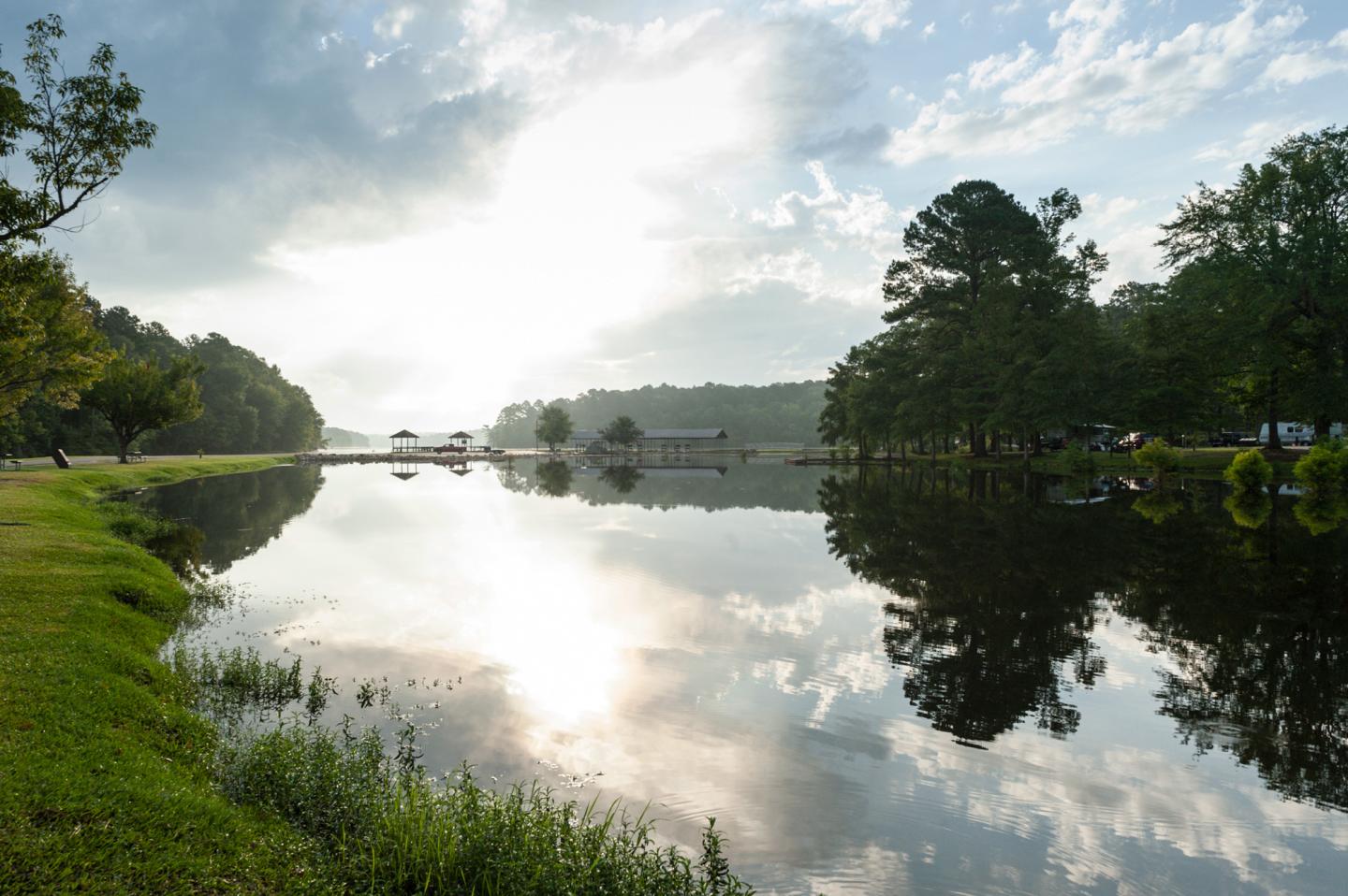 Calm lake reflecting a bright cloudy sky and trees.
