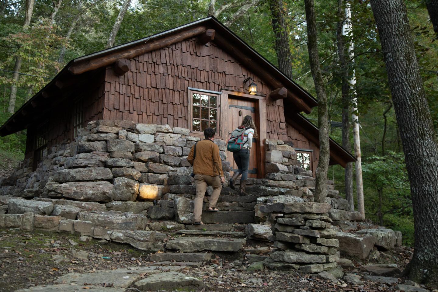 Cozy cabin in the woods with two people entering at dusk.