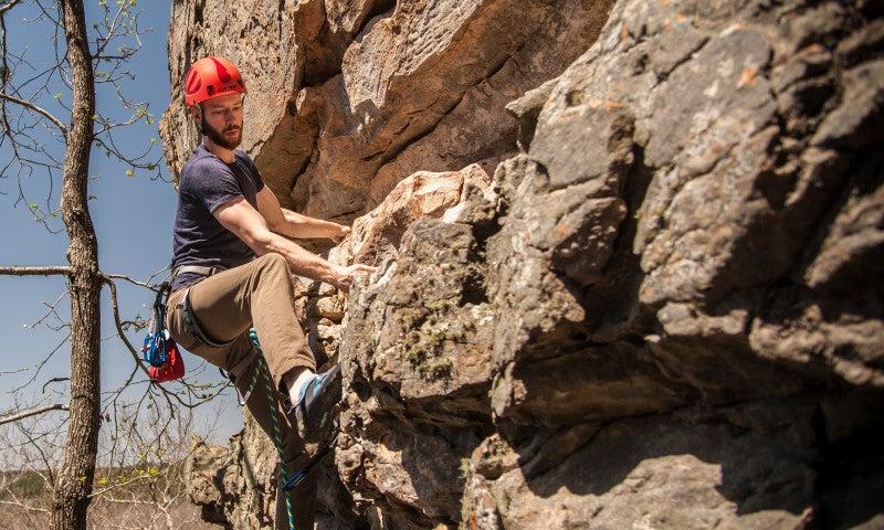 Rock climber with red helmet scaling a cliff in daylight.