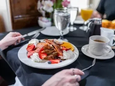 Breakfast with pancakes, bacon, fruit, and coffee on a black tablecloth.