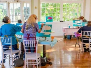 People painting on canvases in a sunlit room.