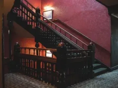 Dimly lit staircase with red textured walls and ornate wooden railing.