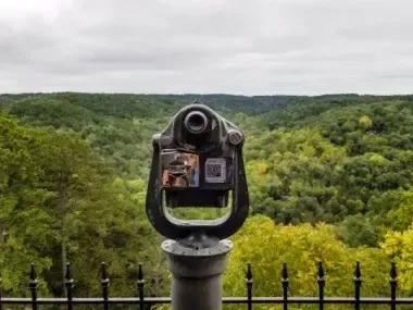 Coin-operated binoculars overlooking a lush green valley.