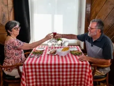 Elderly couple toasting at a table with a red checkered tablecloth.
