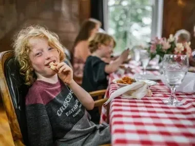Child smiling at a table with a red checkered tablecloth.
