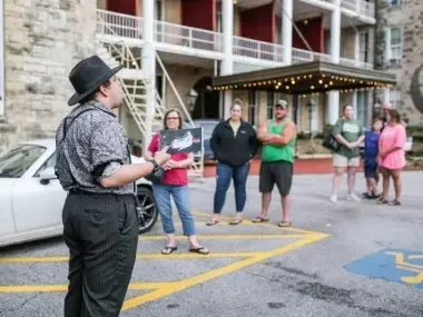 Tour guide in hat speaking to a group outside a building.