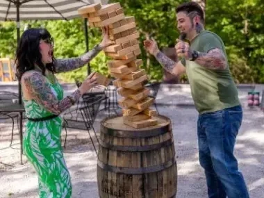 Two people playing giant Jenga outdoors, blocks tilting, both smiling.
