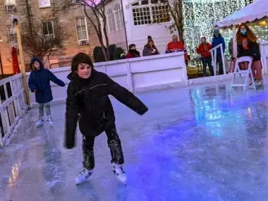 Child ice skating outdoors, evening lights illuminate the scene.