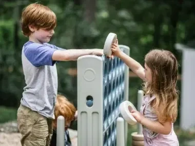 Children playing connect four outdoors with oversized pieces.