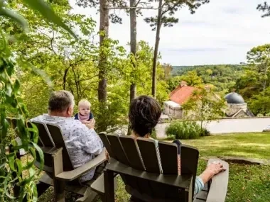Family seated in Adirondack chairs, enjoying a scenic, wooded view.