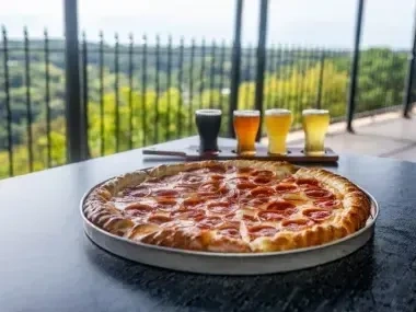 Pizza and beer flight on a balcony with a scenic view.