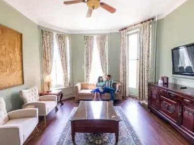 Elegant living room with couple seated on a sofa, large windows, and ornate decor.