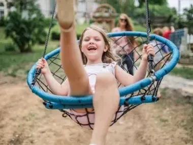 A child joyfully swinging on a round blue net swing in a park.