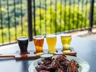 Beer flight and chicken wings on an outdoor table with a scenic view.