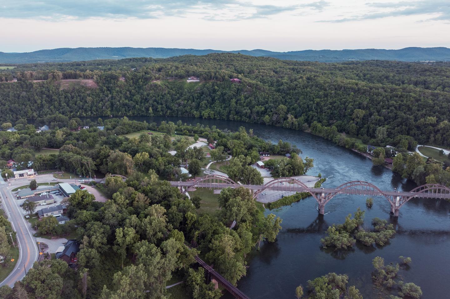 Aerial view of a river with a bridge, surrounded by lush green forest.