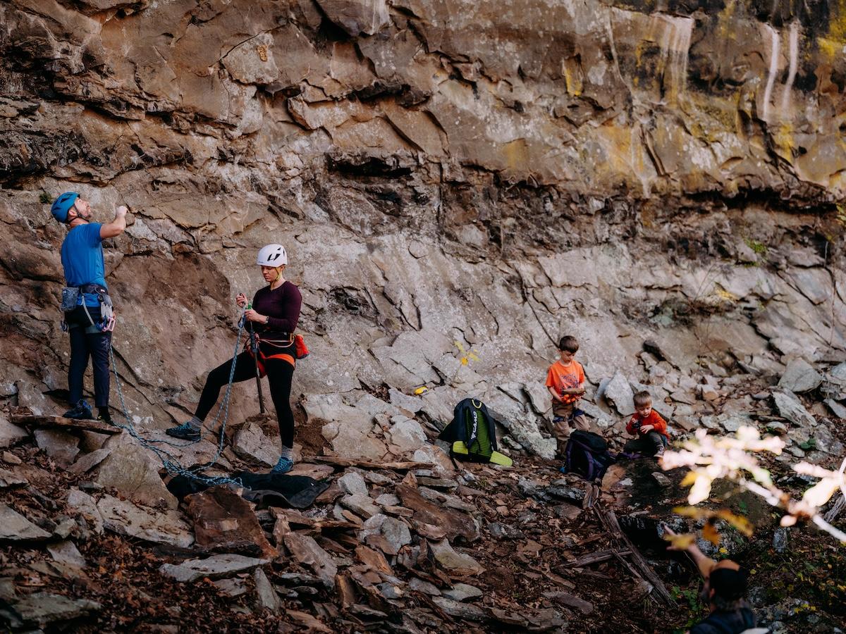 Climbers with helmets gather near a rocky cliffside, preparing gear.