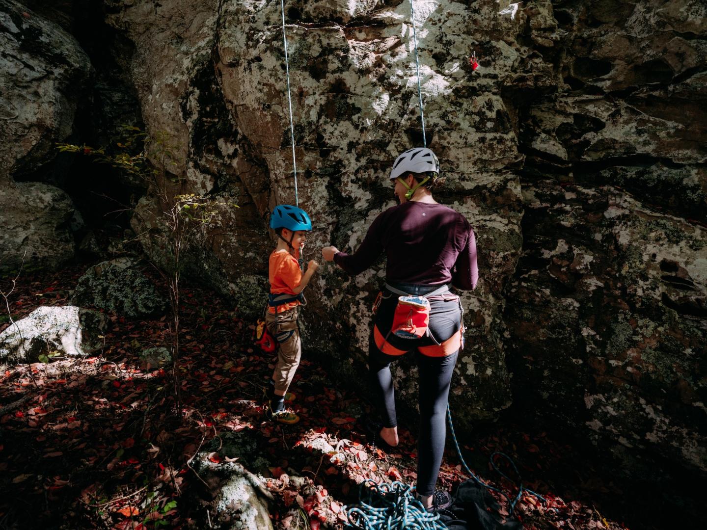 Two people rock climbing, one adult and one child, wearing helmets and harnesses.