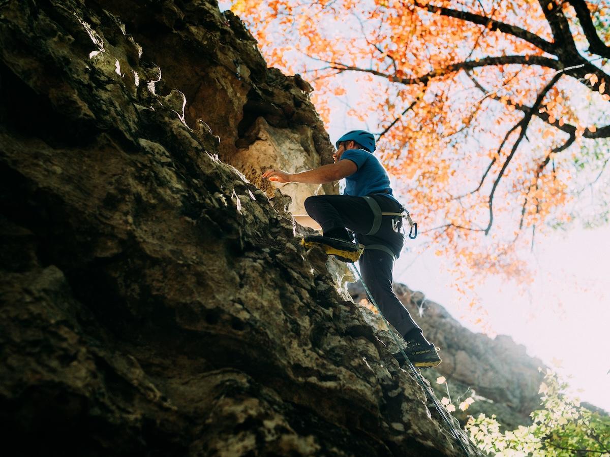 Rock climber ascending a steep cliff, autumn leaves above.