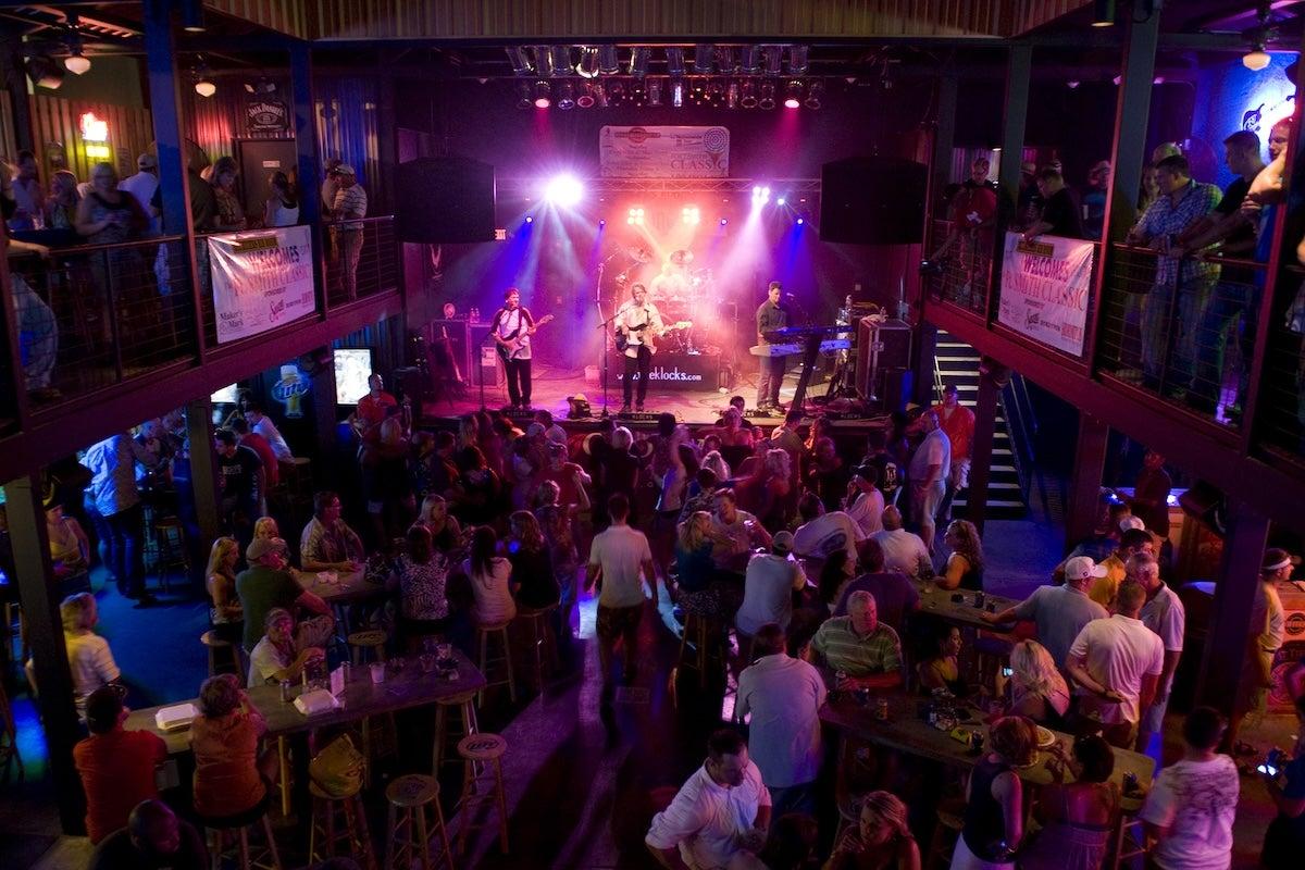 Crowded nightclub with live band under colorful stage lights.