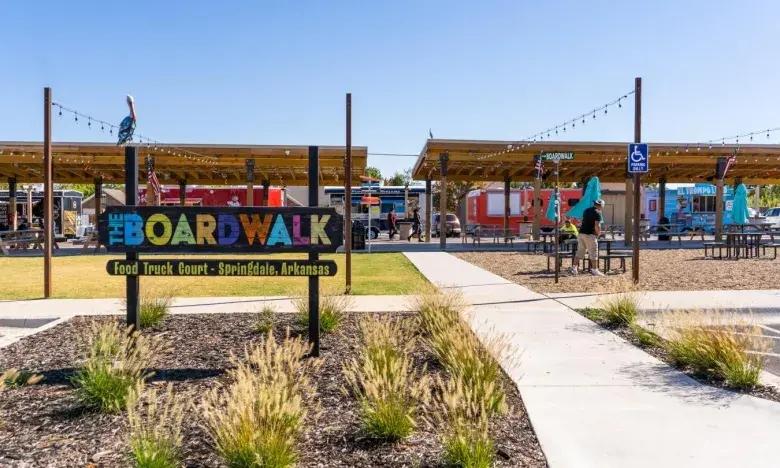 Boardwalk area with colorful stalls and shaded seating under a clear blue sky.