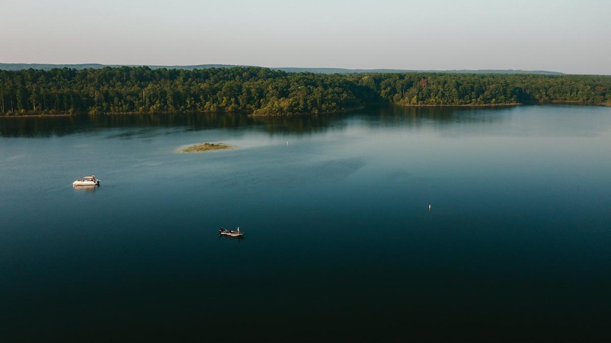 Calm lake with two boats, surrounded by dense forest in the distance.