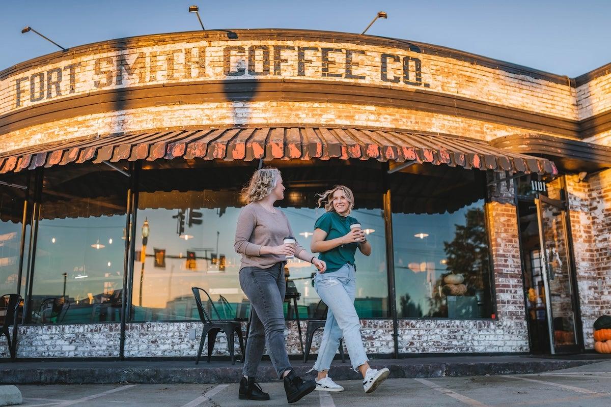 Two people walking happily past a brick coffee shop at sunset.