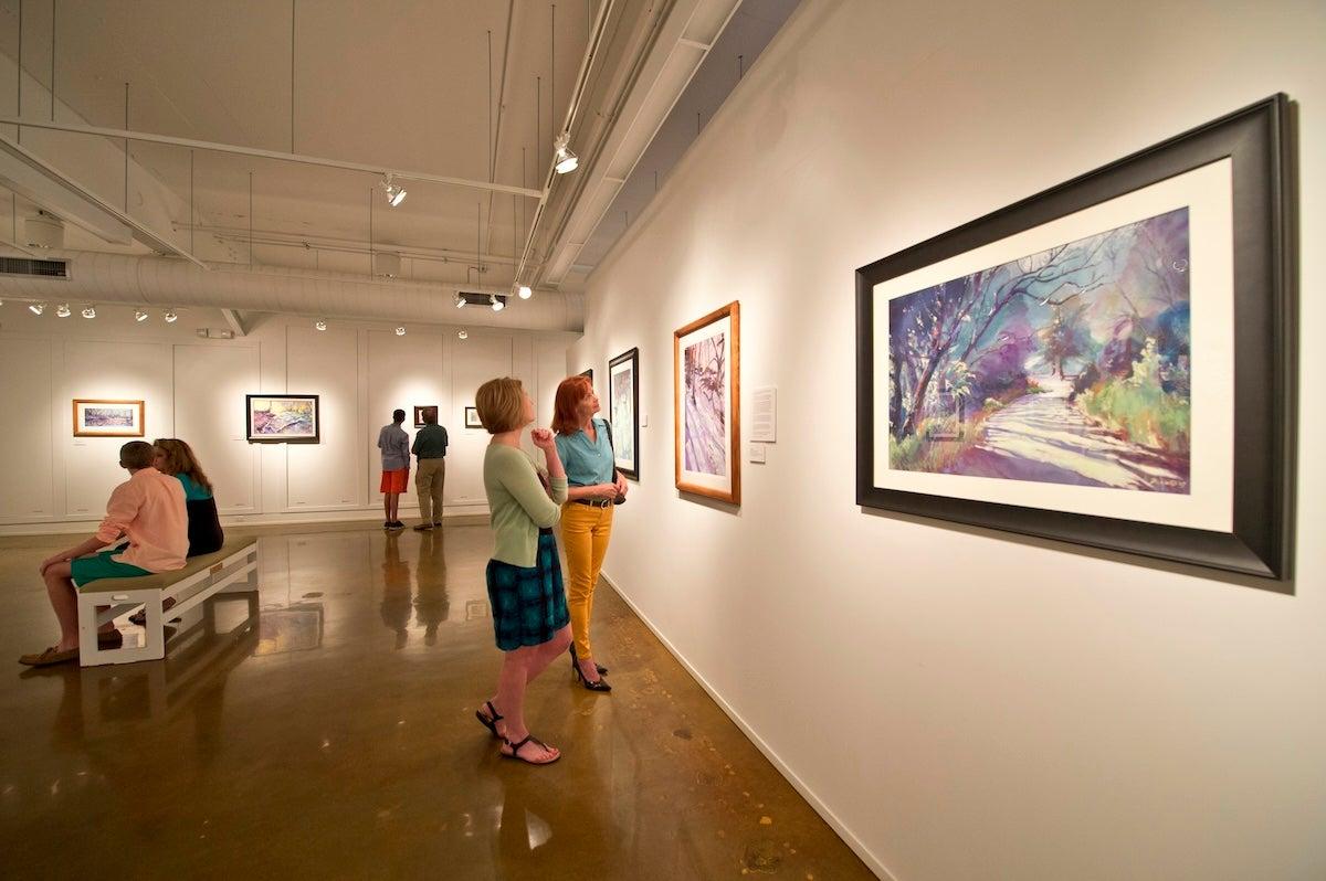 Art gallery with visitors admiring colorful paintings on white walls.
