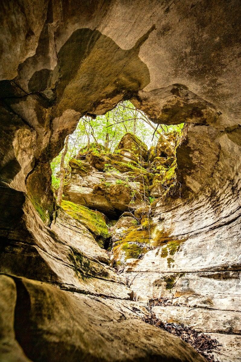 Rocky cave opening with green moss and sunlight above.